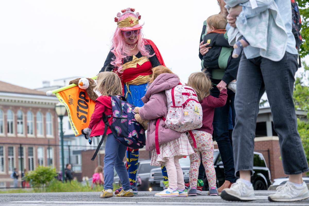 A group of students hug Miss Peggy and pet her animal hand puppets while crossing the street as Miss Peggy controls the traffic at the end of the school day at Washington Elementary School on Tuesday, May 13, 2025, in Tacoma, Wash.