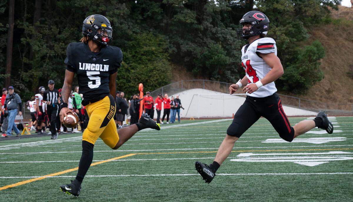 Lincoln quarterback Gabarri Johnson looks back at Camas linebacker Alex Holley as he slips into the end zone for the second of his touchdown runs during Saturday afternoon’s 4A football game at Lincoln Bowl in Tacoma, Washington, on Sept. 17, 2022. Lincoln won the game, 42-28.