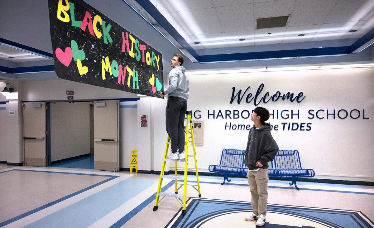 Gig Harbor senior Sam Haddon (left) and junior Ezra Hwang hang a Black History Month banner at the school entrance during the weekly meeting of the Black Student Union at Gig Harbor High School in Gig Harbor, Washington, on Tuesday, Feb. 7, 2023.