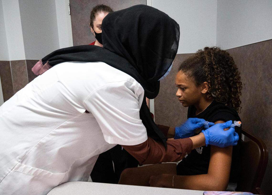 Bartell Drugs head pharmacist Nimo Ahmed, left, administers a dose of the Pfizer vaccine to Makenzie Porter, 11, right, as she holds her mother, Melissa Porter’s, hand at the store in University Place, on Thursday, July 14, 2022.
