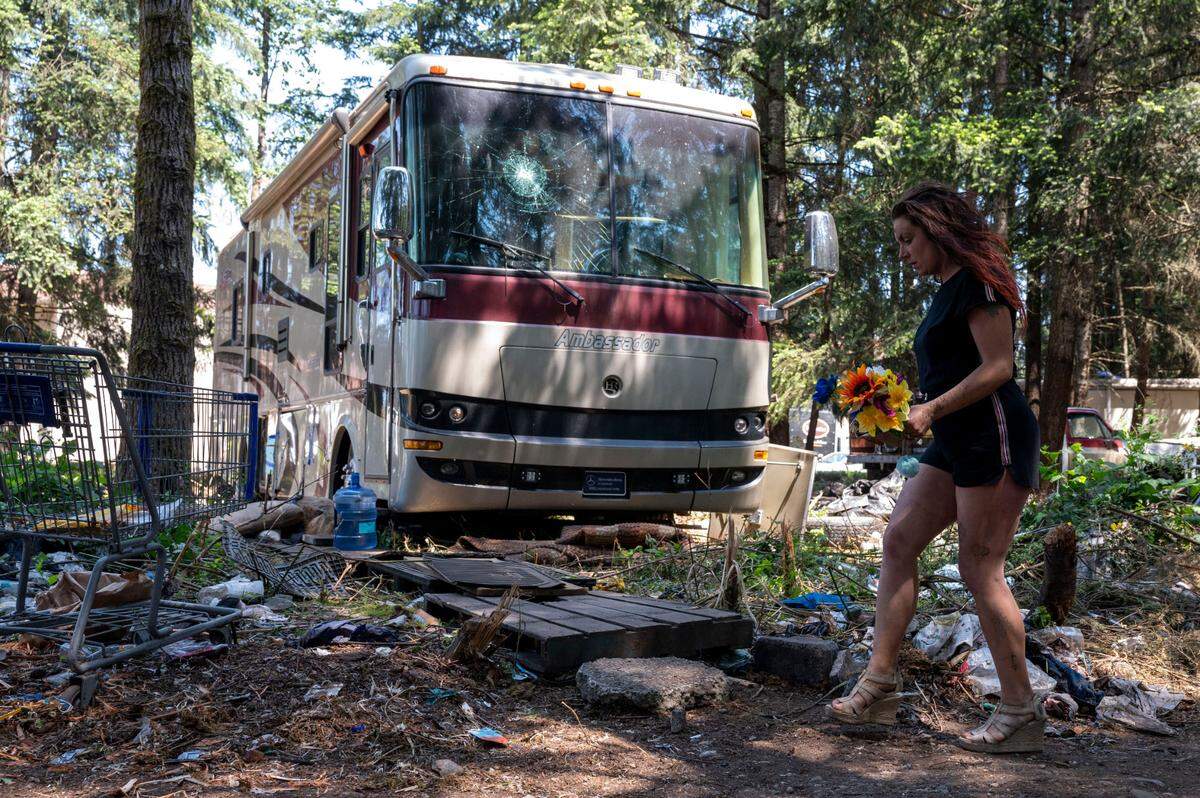 Kelsi Springs, 34, carries a bouquet of fake flowers that was given to her by a friend as she walks past a broken RV at a homeless encampment in the 9700 block of Steele Street South in Tacoma on Thursday, May 25, 2023.