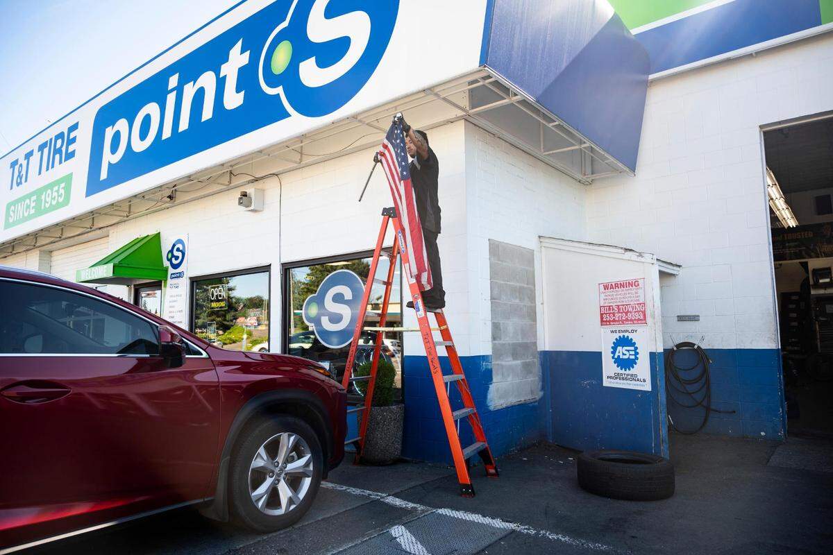 A T&T Tire Point S employee takes down an American flag next to what once was a window that was filled in after being broken during a robbery that occurred at the shop in mid-February, outside of the shop in Tacoma, on Monday, July 11, 2022.