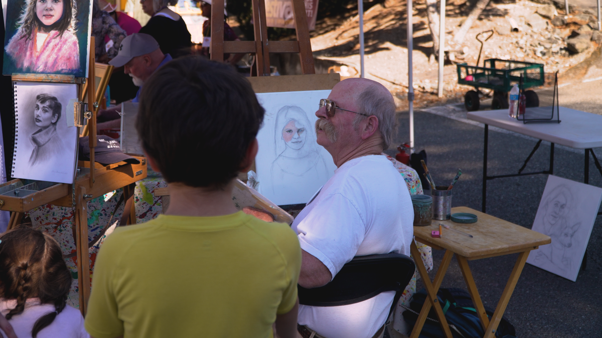 An artist sits by his work on display at the 2023 Summer Art Festival.