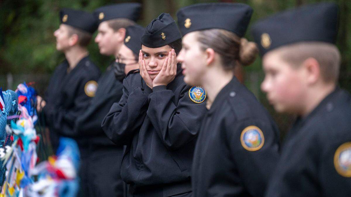 Peninsula Navy National Defense Cadet Corps petty officer second class Abigail Sanchez (center), a freshman a Peninsula High School, attempts to stay warm on a cold morning as they prepare for a Wreaths Across America ceremony at Artondale Cemetery in Gig Harbor, Wash., on Saturday, Dec. 18, 2021.