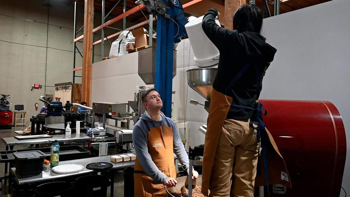 Civic Roasters co-owner Kyle Bradshaw, left, watches as co-owner Benita Ki, right, pours coffee beans into the coffee bean roaster at Roasterworks on Tuesday, April 26, 2022 in Auburn, Wash.