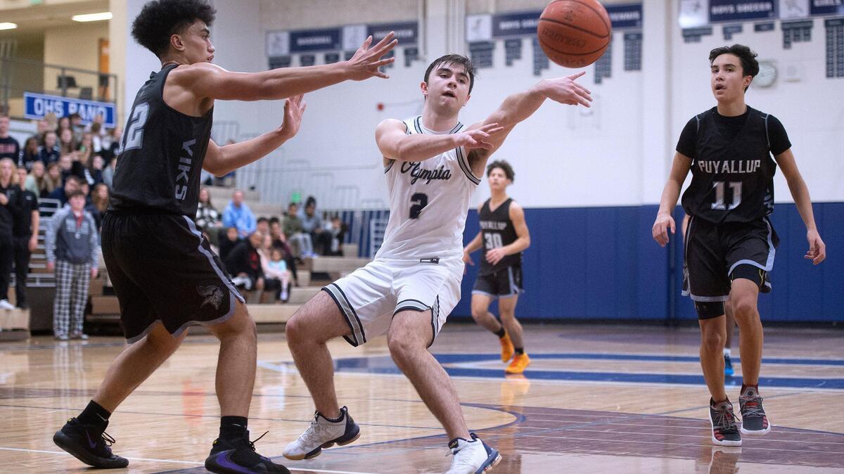 Olympia’s Zack Swanson dishes off a pass between Puyallup defenders LJ Lemalu (left) and Taki Uluilakepa during Saturday night’s SPSL 4A boys basketball game at Olympia High School on Jan. 4, 2020.