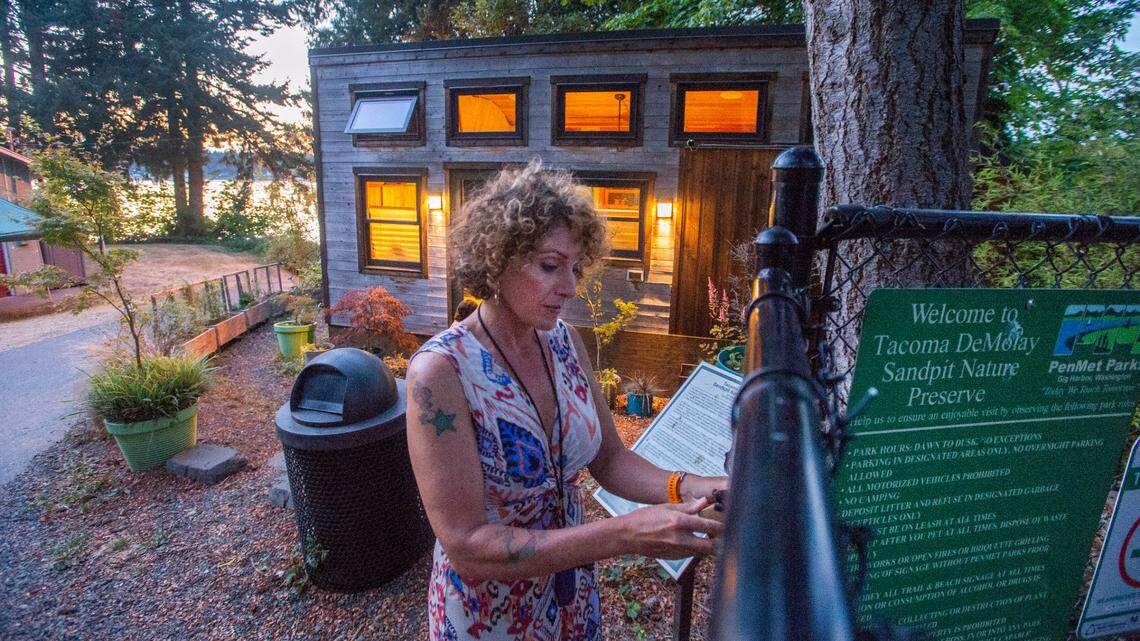 Park host Brett Marlo locks the gate to the DeMolay Sandspit Nature Preserve on Fox Island for the evening Thursday, July 22, 2021. She recently received notification that PenMet Parks is terminating the 17-year-old park host program. Behind her is a 200-foot-square “tiny house” she designed to live on the property that she will be taking with her. The unpaid hosts live rent-free in return for services like opening and closing the park gates, picking up litter, doing some minor maintenance and providing security at night.