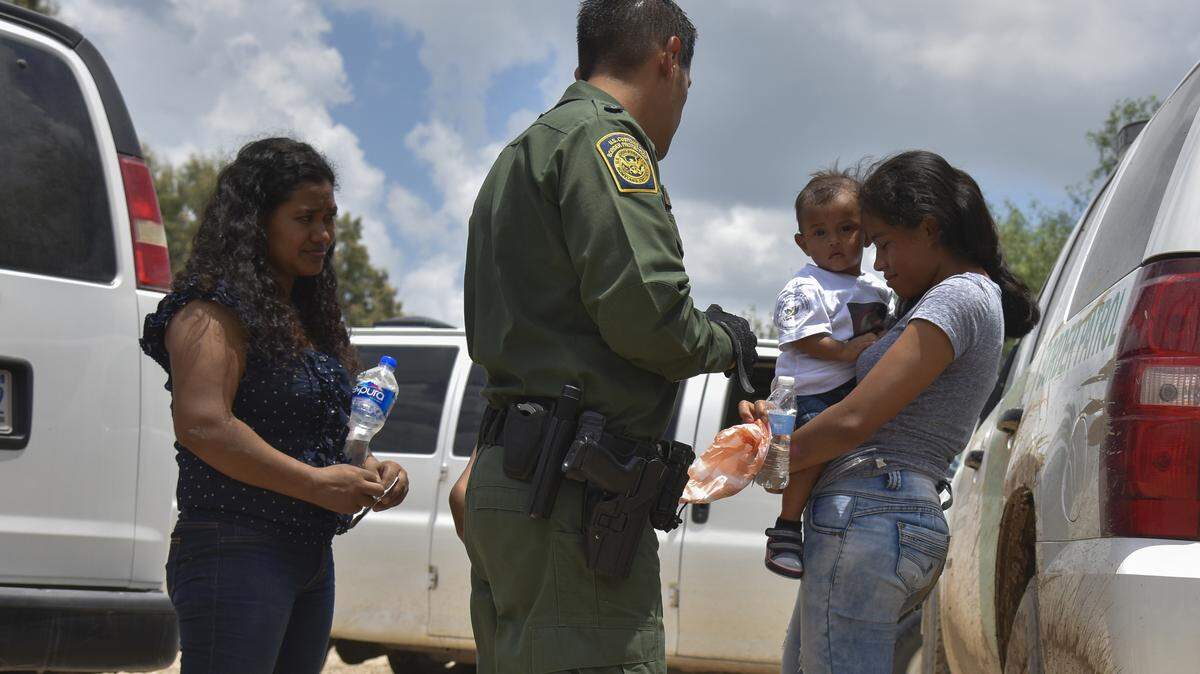 Two mothers from Honduras and their children (a 12-year-old, blocked from view, and a 1-year-old shown here) are detained by a Border Patrol agent in Texas after rafting across the Rio Grande.