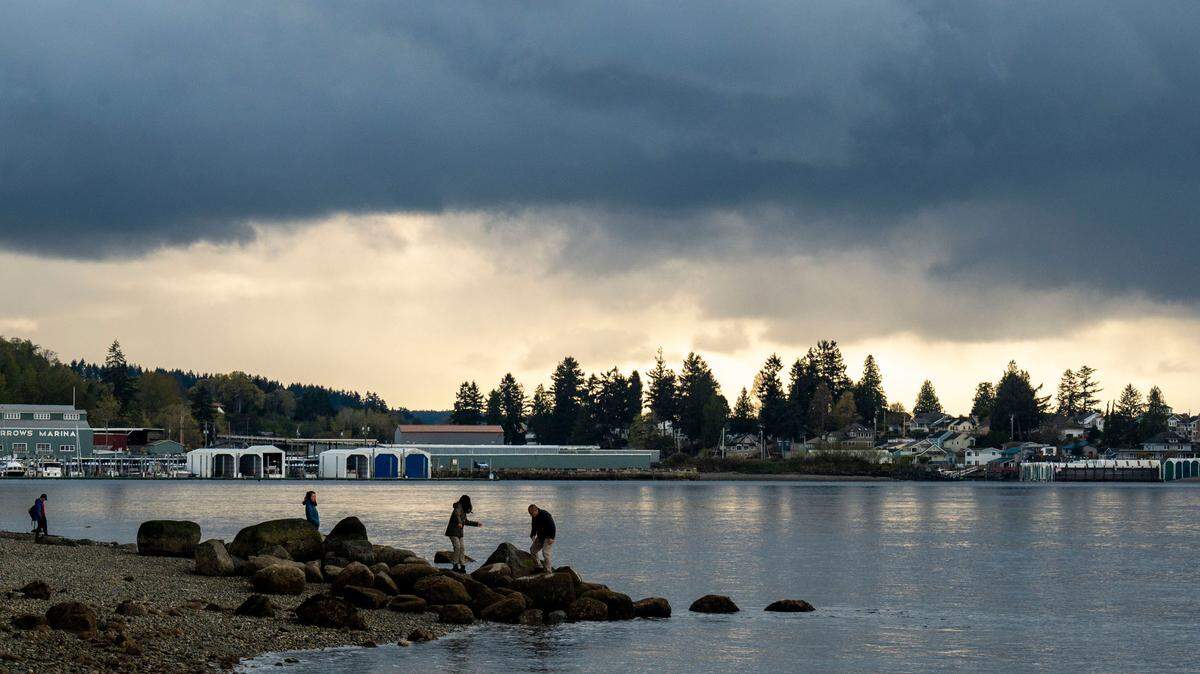 Rain clouds roll over University Place, Wash. as people walk along the rocks at Titlow Beach on Tuesday, April 12, 2022.