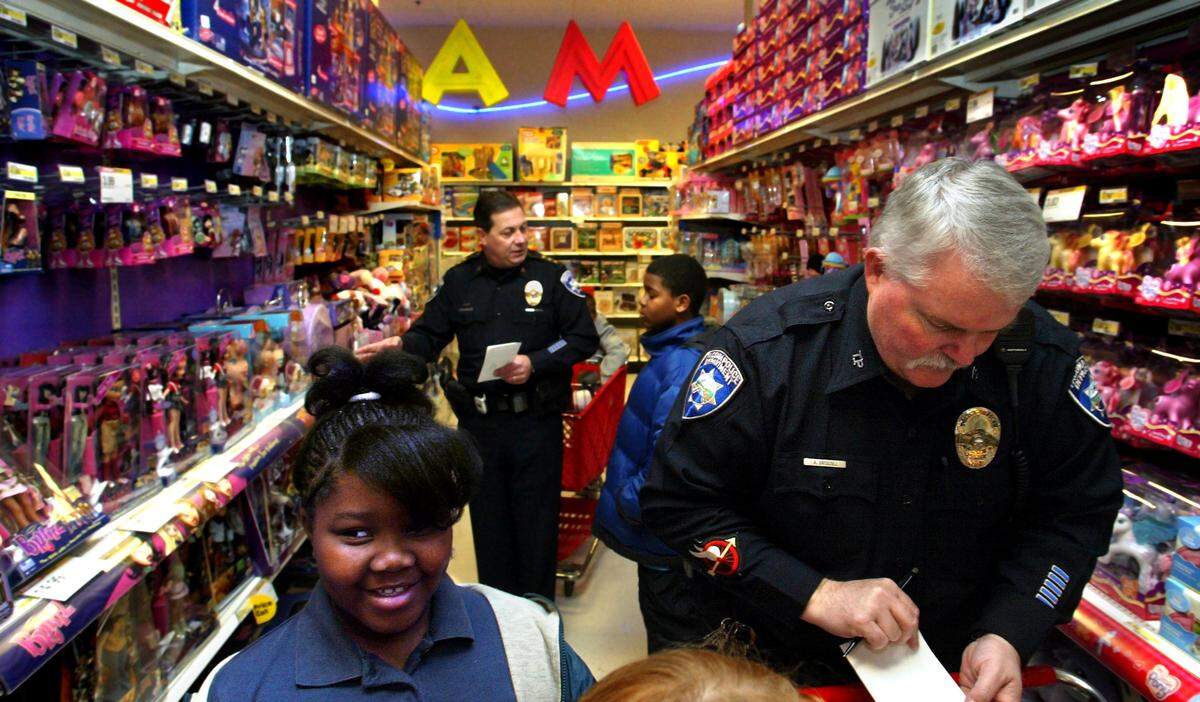 While Tacoma Police Patrol Officer Tony Driscoll kept track of her purchases Kameisha Williams 10, left, eyed other toys during the 15th annual ‘Shop with a Tacoma Cop,’ program held at he Union Street Target Store in Dec. 2004. Approx. 70 PD officers participated this year showing up at 7a.m. before the store opened to te public to shop with area underprivileged kids ages 7 to 11 yrs, old. Tacoma Police Chief Don Ramsdell center shops with Thomas Jones, 10, of Tacoma in the background.