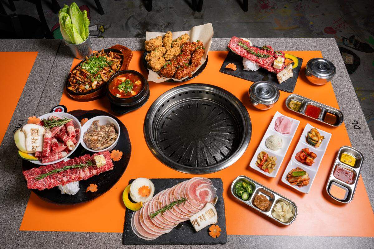 Selections from Mukja Korean BBQ’s menu are laid out around a table grill at the restaurant on Friday, April 18, 2025, in Puyallup, Wash. Included are, clockwise from left, a Mukja Beef Combo, or Combo C, lettuce, stir fried squid, kimchi stew, Korean fried chicken, half made sweet and spicy, boneless short rib, containers of rice, dipping sauces and sides including sesame oil, chili sauce, meat sauce, fish cakes, potato salad, kimchi variations and soy bean paste, and thinly sliced pork belly.