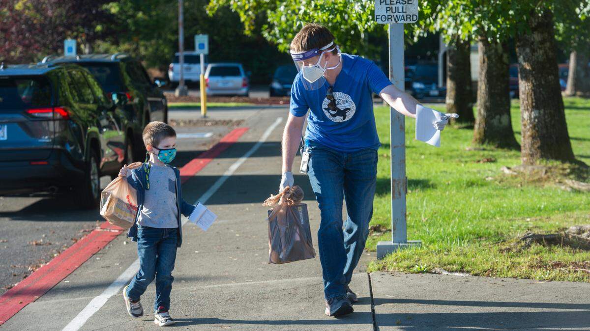 Substitute teacher Welsey Mosier helps guide a student toward a temperature screening station at Harbor Heights Elementary in Gig Harbor Monday, Sept. 28, 2020. It was the first day of in-person instruction for kindergarten and first grade students in the Peninsula School District.