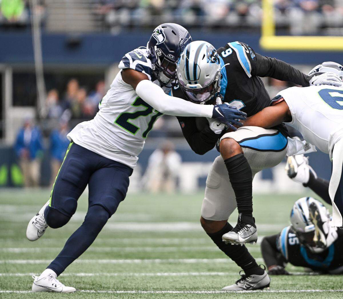 Carolina Panthers running back Miles Sanders (6) is tackled by Seattle Seahawks cornerback Devon Witherspoon (21) and Seattle Seahawks safety Quandre Diggs (6) during the first quarter of the game at Lumen Field, Sunday, Sept. 24, 2023, Seattle, Wash.