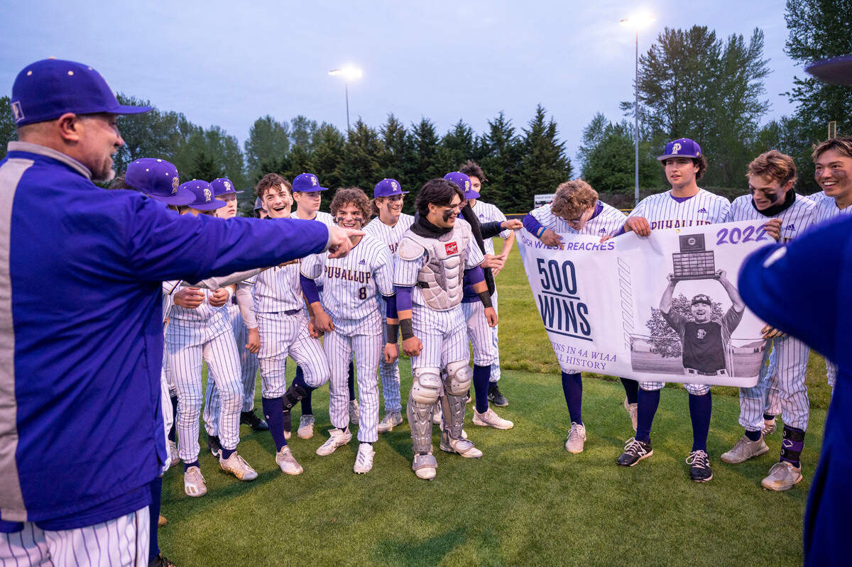 Puyallup head coach Marc Wiese points to a banner that players were holding up after the team beat Graham-Kapowsin, 10-0, to earn Wiese his 500th win on Tuesday, May 3, 2022, at Heritage Park in Puyallup.