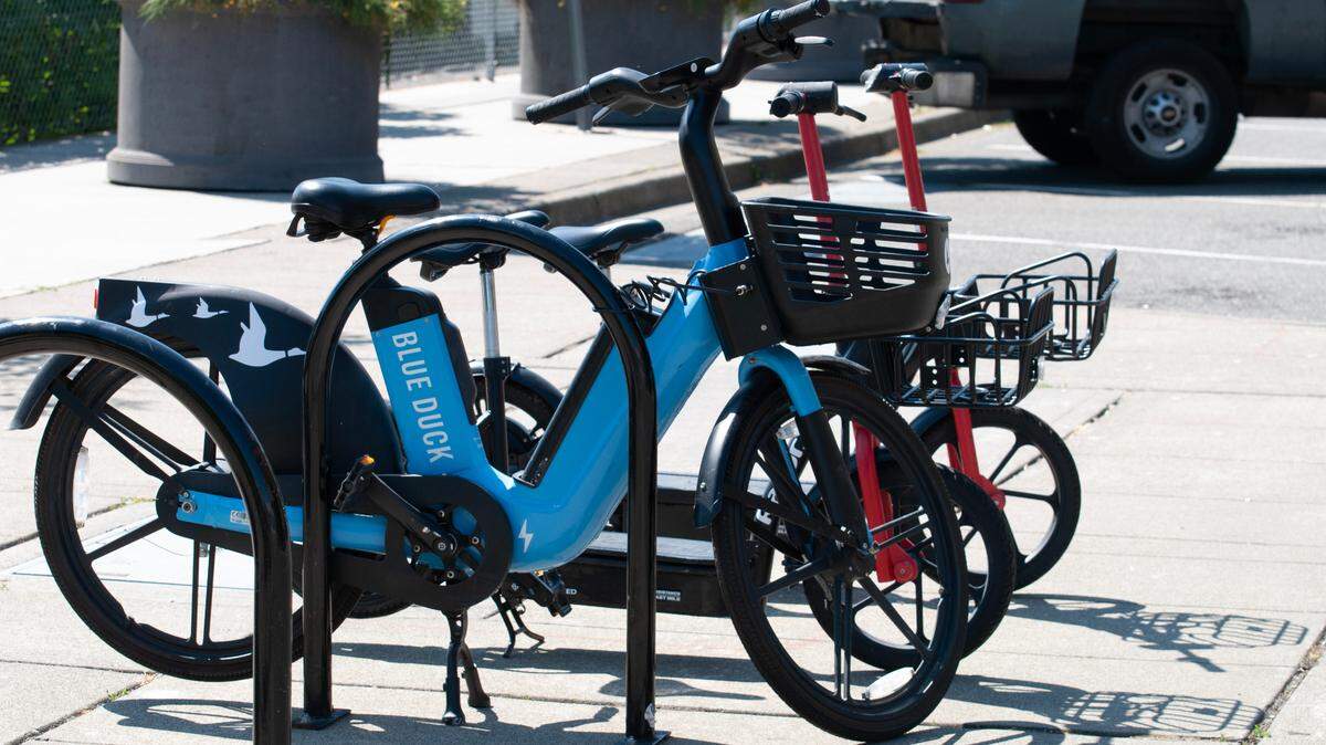 One of Tacoma’s newly released e-bikes with two electric scooters behind it on Broadway in downtown Tacoma on June 28, 2023.