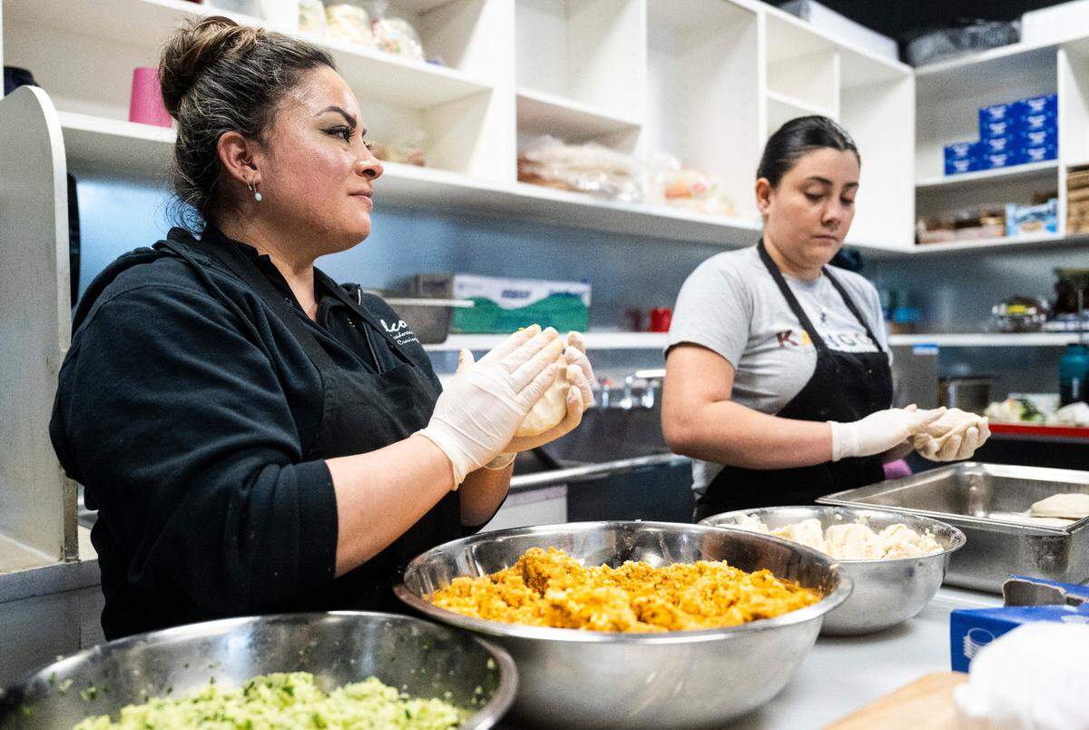Ofelia Amaya, left, shows her technique for making pupusas at Balcon Express in Tacoma on Jan. 18, 2023. She rolls masa around the filling into the shape of a small football, then flattens into discs, while Ingrid (right) starts with a dumpling-like shape.