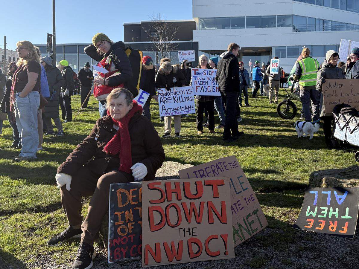 A woman sits among protestors with signs advocating to shut down the Northwest Detention Center at the anti-Trump rally at Fireman’s Park on Saturday, January 24, 2026.