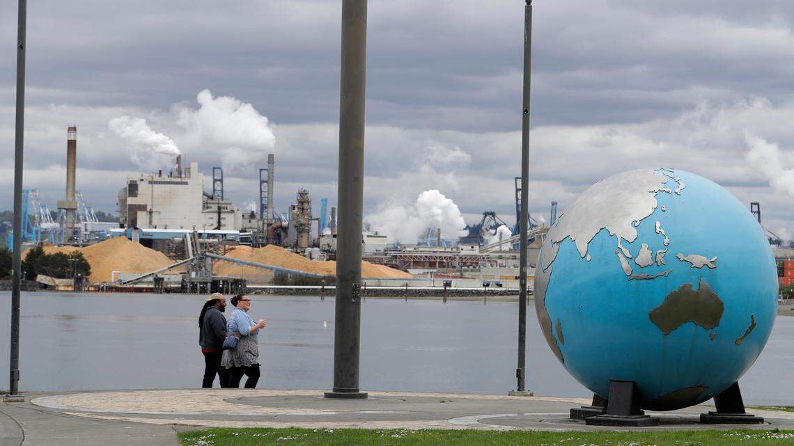 In this April 21, 2020 photo, people walk past an Earth globe sculpture at Thea’s Park in Tacoma, Wash., with the WestRock Paper Mill in the background. (AP Photo/Ted S. Warren)