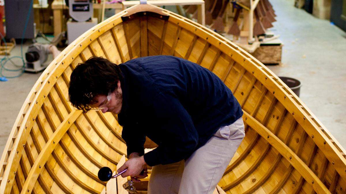 A student works on a wooden boat like the one BoatShop students will build this fall.