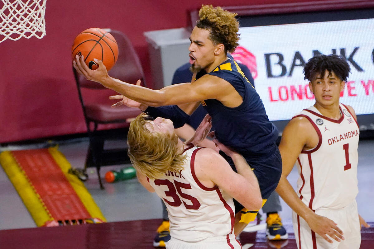 West Virginia forward Emmitt Matthews Jr., center, collides with Oklahoma forward Brady Manek (35) as he goes to the basket in the second half of an NCAA college basketball game Saturday, Jan. 2, 2021, in Norman, Okla. Manek was called for a foul on the play. (AP Photo/Sue Ogrocki)