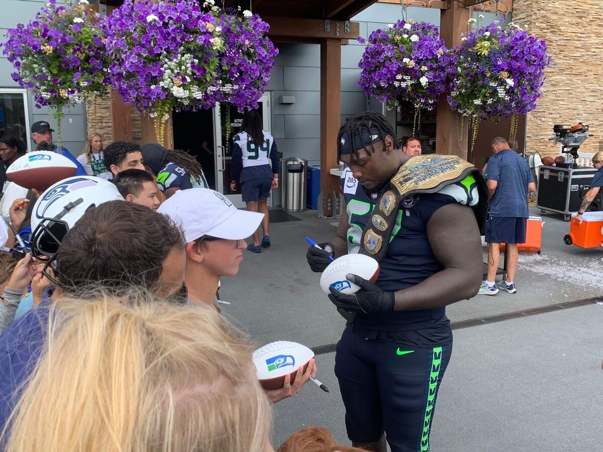 Left tackle Charles Cross (67) signing autographs for fans while wearing the championship belt the coaches and teammates give to a member of the Seahawks’ unit that wins the day in scrimmaging during training camp, on July 30, 2024, at the Virginia Mason Athletic Center in Renton.