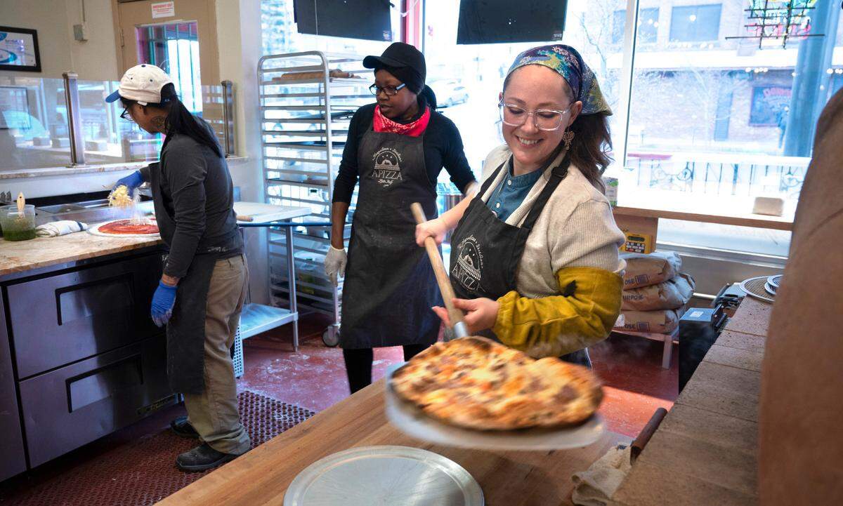 General manager Cassi Curtis pulls an off-menu pizza (the Napoli with salami, artichoke hearts, roasted red peppers and pepperonicinis) from the gas-fired clay oven at APIZZA Little Italy in downtown Tacoma, Washington, on Thursday, March 9, 2023.
