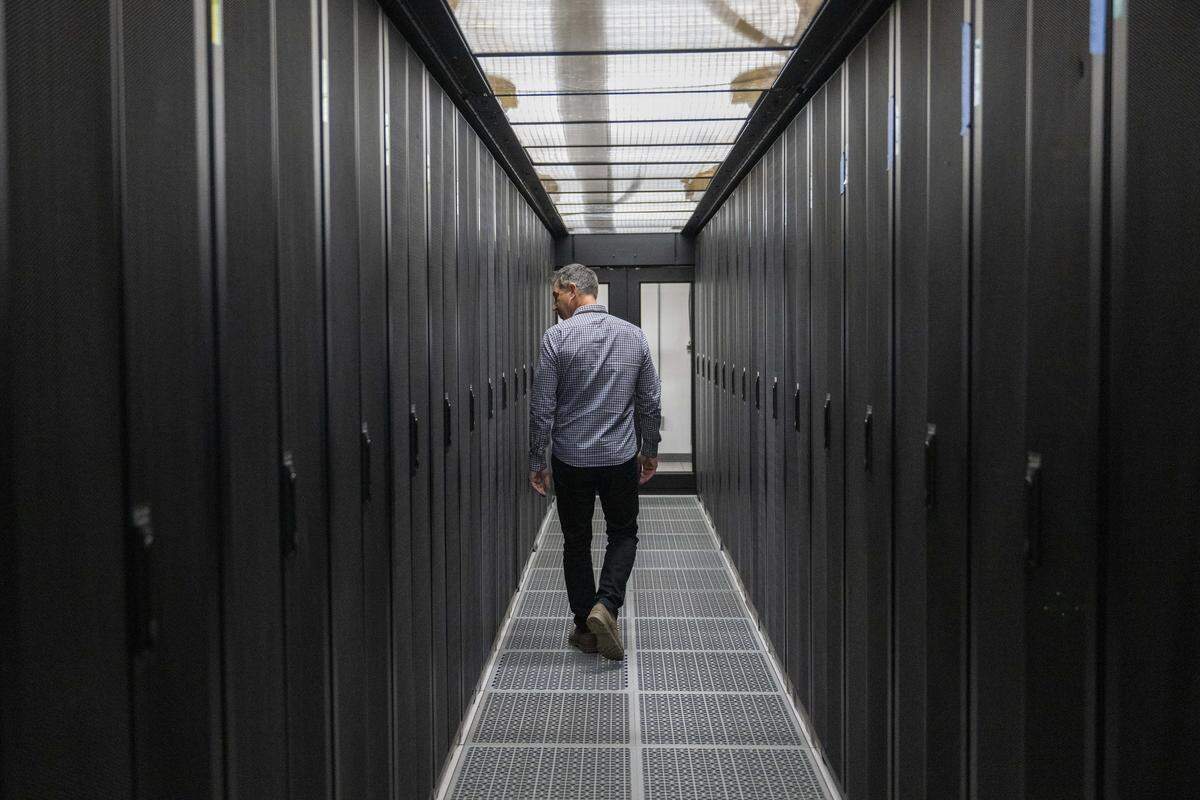 Dave Vranizan, Centeris vice president of leasing and operations, walks along an enclosed corridor of server racks on Friday, Feb. 13, 2026, at the SH1 Data Center in Puyallup, Wash. Air is circulated through grates on the floor to maintain temperatures in the space.