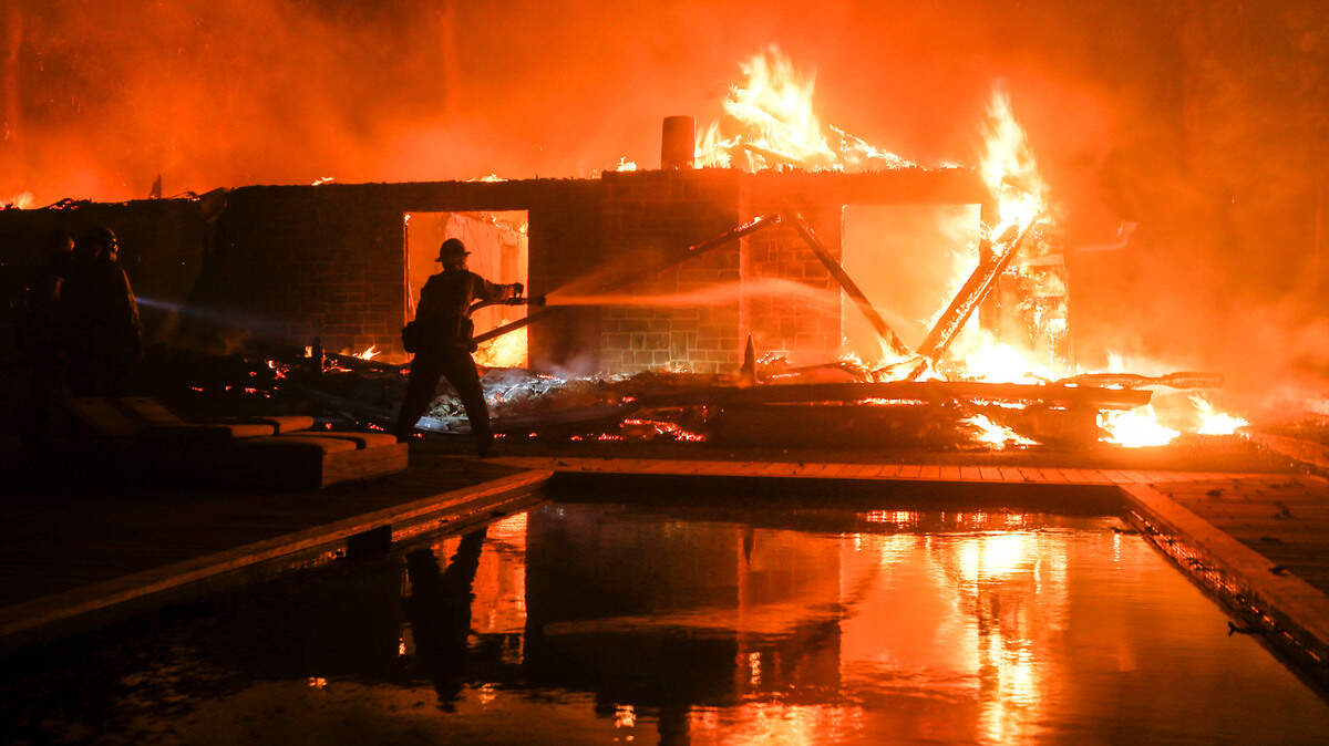 FILE - In this Friday, Nov. 9, 2018 file photo, a firefighter battles the Woolsey Fire burning a home in Malibu, Calif. Fire officials announced Wednesday evening, Nov. 21, that the Woolsey Fire is 100 percent contained. The wind-whipped blaze erupted on Nov. 8 and spread destruction from Thousand Oaks to Malibu, west of Los Angeles. (AP Photo/Ringo H.W. Chiu, File)