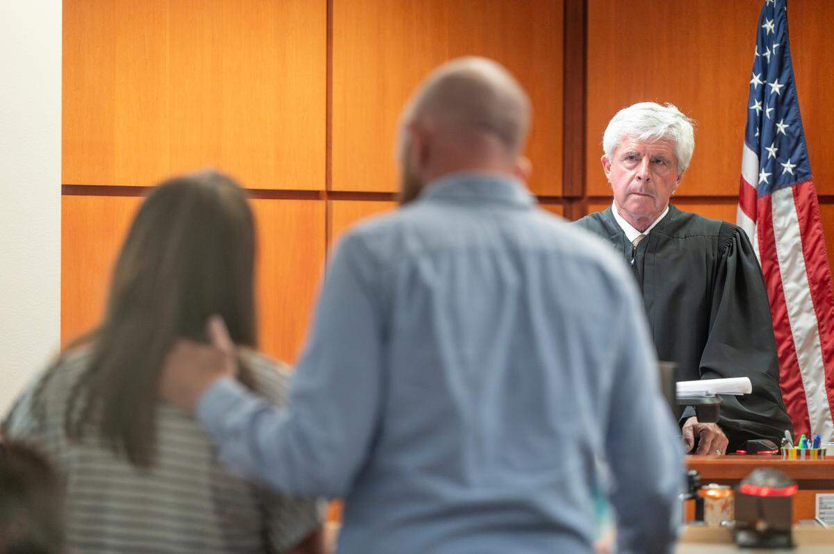 Foster parents Kelli, left, and Robert Higginbotham give a statement to Pierce County Superior Court Judge Stanley Rumbaugh, right, at a plea hearing and sentencing for Ivey Lewis on Thursday, July 3, 2025, in Tacoma. Lewis plead guilty to charges of homicide by abuse for beating her 3-year-old son and foster child to the Higginbothams, Prince Lewis, to death.