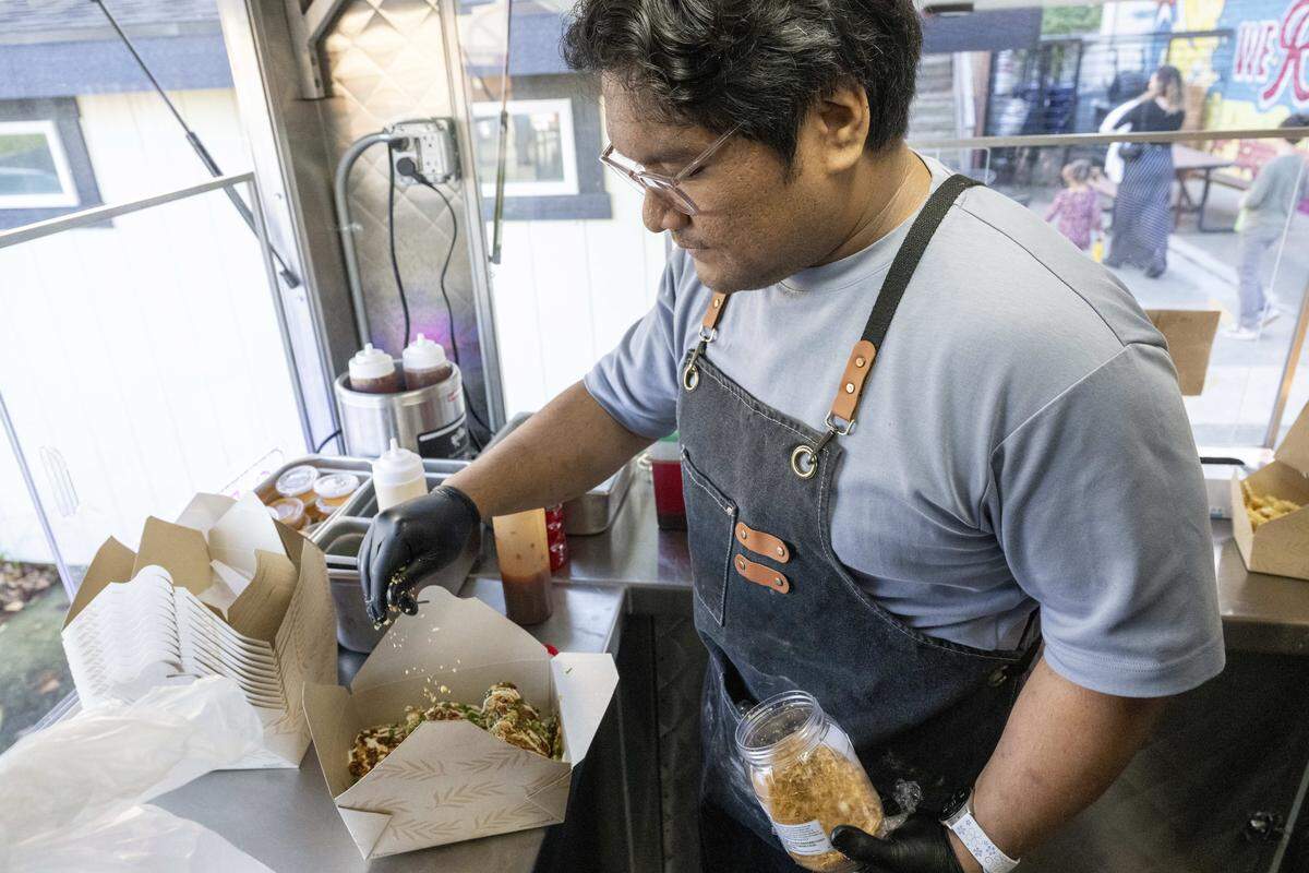 Franco Magofna, head chef of The Chicken Supply Tacoma location, sprinkles fried garlic on an order of chicken thighs loaded with a soy lemon aioli on Wednesday, Oct. 29, 2025, in Tacoma, Wash.