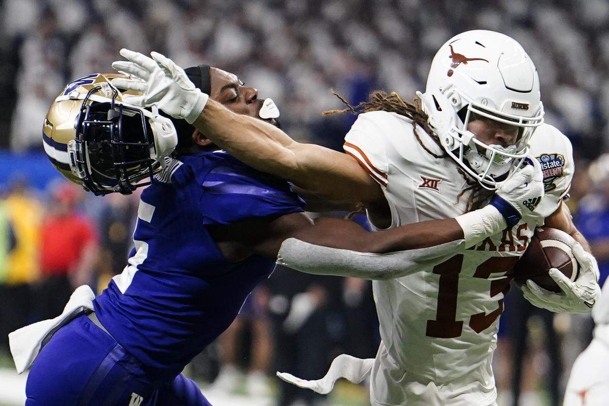 The Texas wide receiver Jordan Whittington (13) runs against Washington linebacker Edefuan Ulofoshio (5) removing his helmet on the run during the first half of the Sugar Bowl CFP NCAA semifinal college football game, Monday, Jan. 1, 2024, in New Orleans. (AP Photo/Jacob Kupferman)