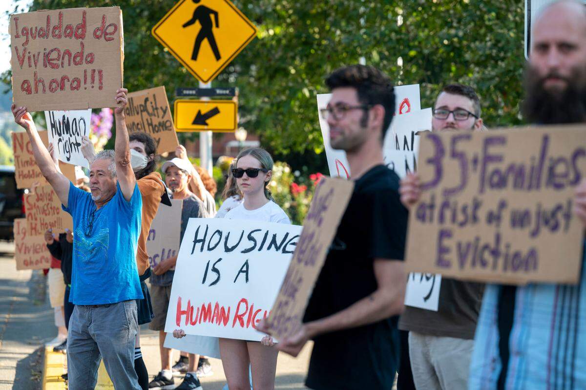 Armando Aragon (left) holds up a sign that reads “equal living now” in Spanish while at a rally in support of the residents of Meridian Mobile Estates prior to a Puyallup City Council meeting on Tuesday, August 23, 2022, at Pioneer Park in Puyallup, Wash.