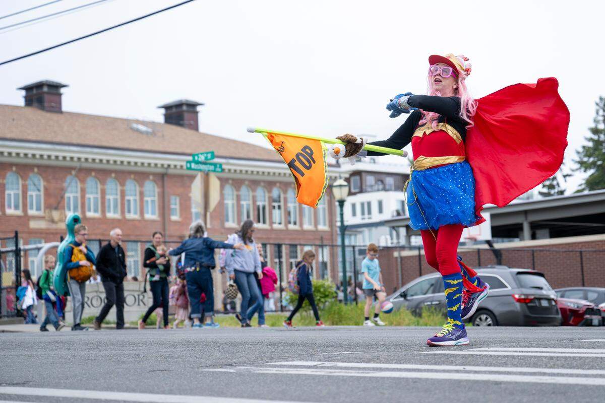 The cape of Miss Peggy’s Wonder Woman costume catches in the wind as she moves to stop traffic at an intersection by Washington Elementary School at the end of the day on Tuesday, May 13, 2025, in Tacoma, Wash.