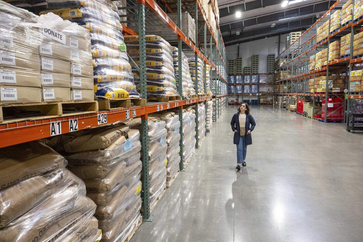 Claire Aijian, development director with Emergency Food Network, walks down an aisle of food storage at a warehouse for the EFN on Tuesday, Oct. 28, 2025, in Tacoma, Wash.