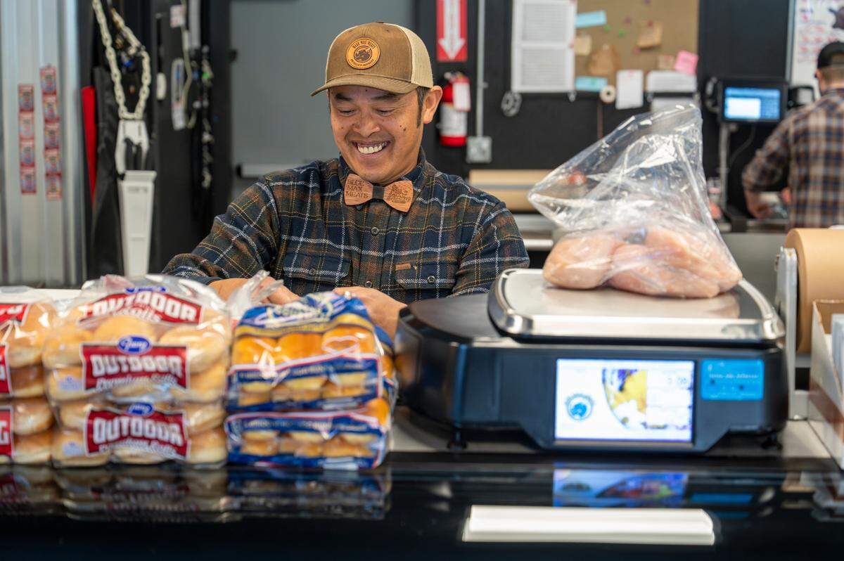 Mapp Chhim, director of operations at Blue Max Meats, smiles while weighing out chicken for a customer just after the shop opened on May 21. While the quality is consistent, friendly customer service keeps customers coming back.