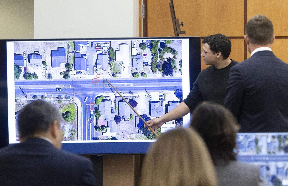Witness Seth Cowden, who filmed a video of the beating and killing of Manny Ellis, points to where he says a Tacoma police officerÕs car was parked in an aerial view of the scene, shot later. The larger circle at left is where someone else said it was parked. The map is projected onto a screen during the Ellis trial in Pierce County Superior Court Wednesday, Oct. 18, 2023, in Tacoma, Wash. Tacoma Police Officers Christopher Burbank, Matthew Collins and Timothy Rankine are on trial for his death. At right is defense attorney attorney Casey Arbenz. Cowden shot the video from a parked car on the street on the right side of the T formation of the streets where there is another circle. (Ellen M. Banner / Pool / The Seattle Times)