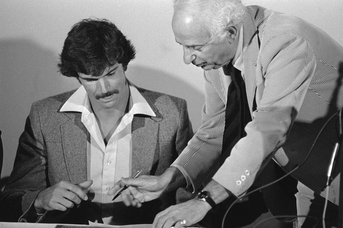 Danny Vranes, No. 1 draft choice of the Seattle Super Sonics on June 8, gets set to sign his contract with the NBA club at a news conference on Wednesday, July 8, 1981 in Seattle. Standing over Vranes with pen in hand is Zollie Volchok, Sonics general manager.