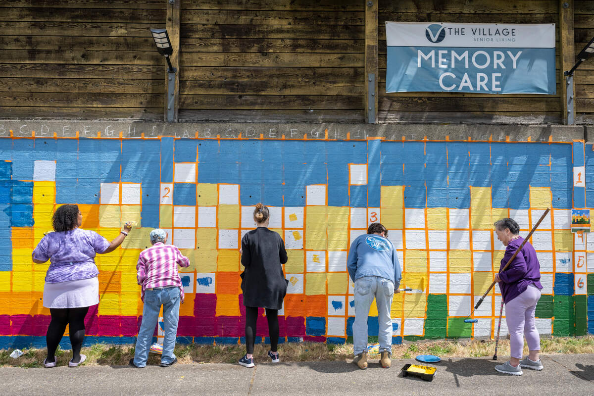 Residents and staff at The Village Senior Living paint a mural on Friday, June 20, 2025, outside of the assisted living facility in Tacoma, Wash. The mural, depicting Mount Tahoma, or Mount Rainier, at sunset, covers graffiti that was previously on the wall, while partnering with The Longest Day Alzheimer’s Association to raise money and awareness for the disease.
