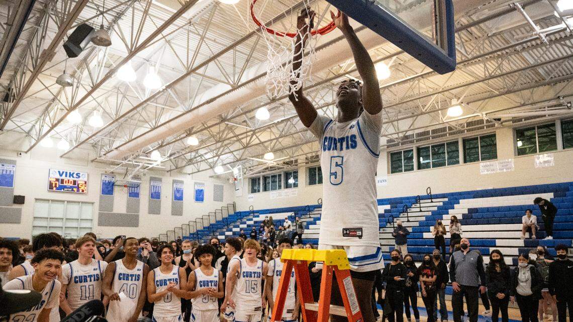 Curtis’s guard Zoom Diallo (5) cuts down a piece of the net as his teammates watch after winning the 4A District 3/4 high school boys basketball championship game at the Curtis High School on Saturday, Feb. 19, 2022, in University Place, Wash.