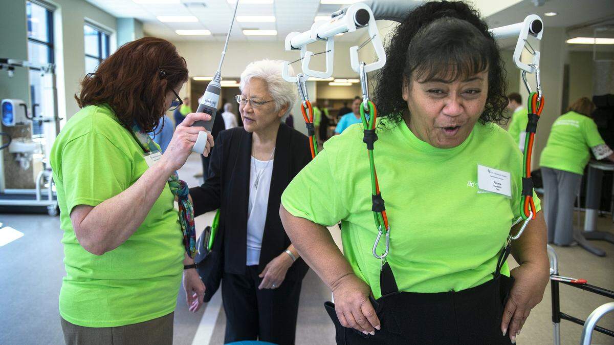 Aloma Meredith, a certified nursing assistant from Tacoma, tries out the ceiling unloading system as physical therapist Mary Eileen Barr (left) explains the system to Sister Rochelle Liu in the rehabilitation gym at the new CHI Franciscan Health Rehabilitation Hospital in Tacoma during an open house in May. The hospital in June received certification from the Joint Commission.
