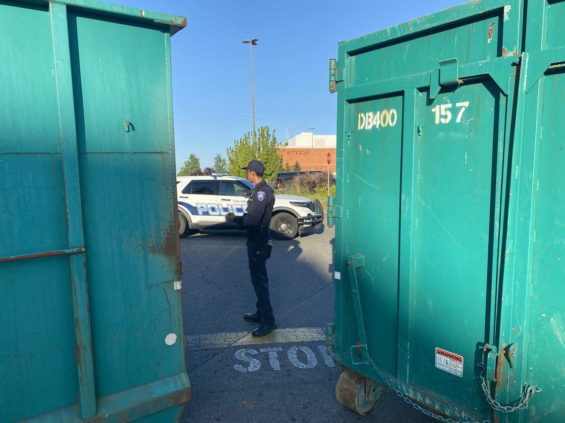 A Tacoma police officer stands guard between two garbage dumpsters set up to block access to the Tacoma Mall parking lot Monday evening. Police blocked all entrances surrounding the mall as protests took place in the city.
