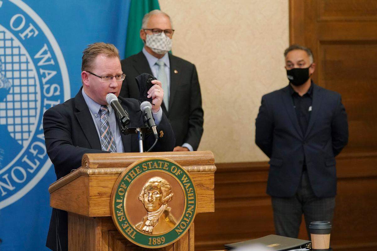 Washington State Superintendent of Public Instruction Chris Reykdal, left, holds up a face mask as he speaks at a news conference, along with Gov. Jay Inslee and Secretary of Health Umair A. Shah at the Capitol, Wednesday, Aug. 18, in Olympia. Inslee announced that Washington state is expanding its vaccine mandate to include all public, charter and private school teachers and staff, as well as those working at the state’s colleges and universities. The Governor also expanded the statewide indoor mask mandate in place for non-vaccinated individuals to include those who are vaccinated.