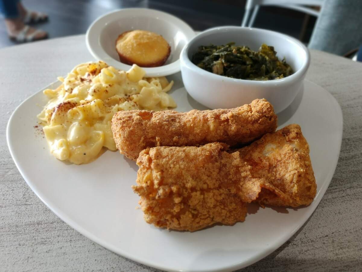 A fried fish dinner with cod, macaroni and cheese and collard greens.