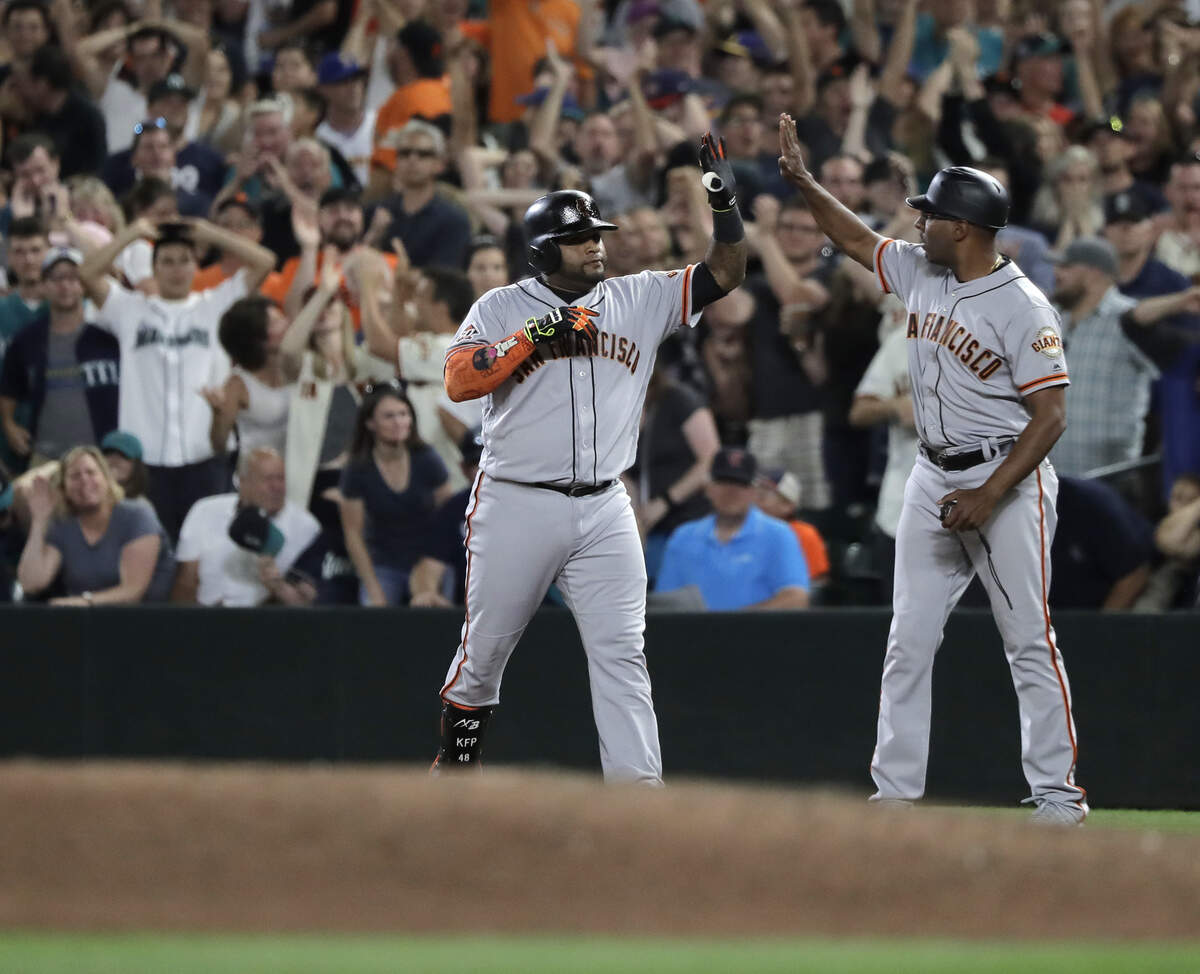 San Francisco Giants' Pablo Sandoval, left, is greeted by first base coach Jose Alguacil, right, after Sandoval reached on a throwing error by Seattle Mariners second baseman Dee Gordon and Giants' Steve Duggar scored during the ninth inning of a baseball game Tuesday, July 24, 2018, in Seattle. The Giants won 4-3. (AP Photo/Ted S. Warren)