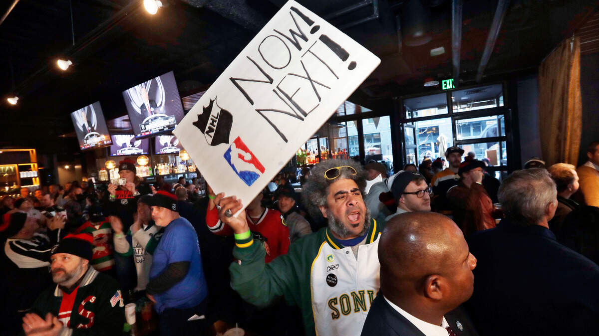 The late Kris “Sonic Guy” Brannon holds up a sign in support of adding an NBA team following the announcement of a new NHL hockey team in Seattle, at a celebratory party Tuesday, Dec. 4, 2018, in Seattle. (AP Photo/Elaine Thompson)