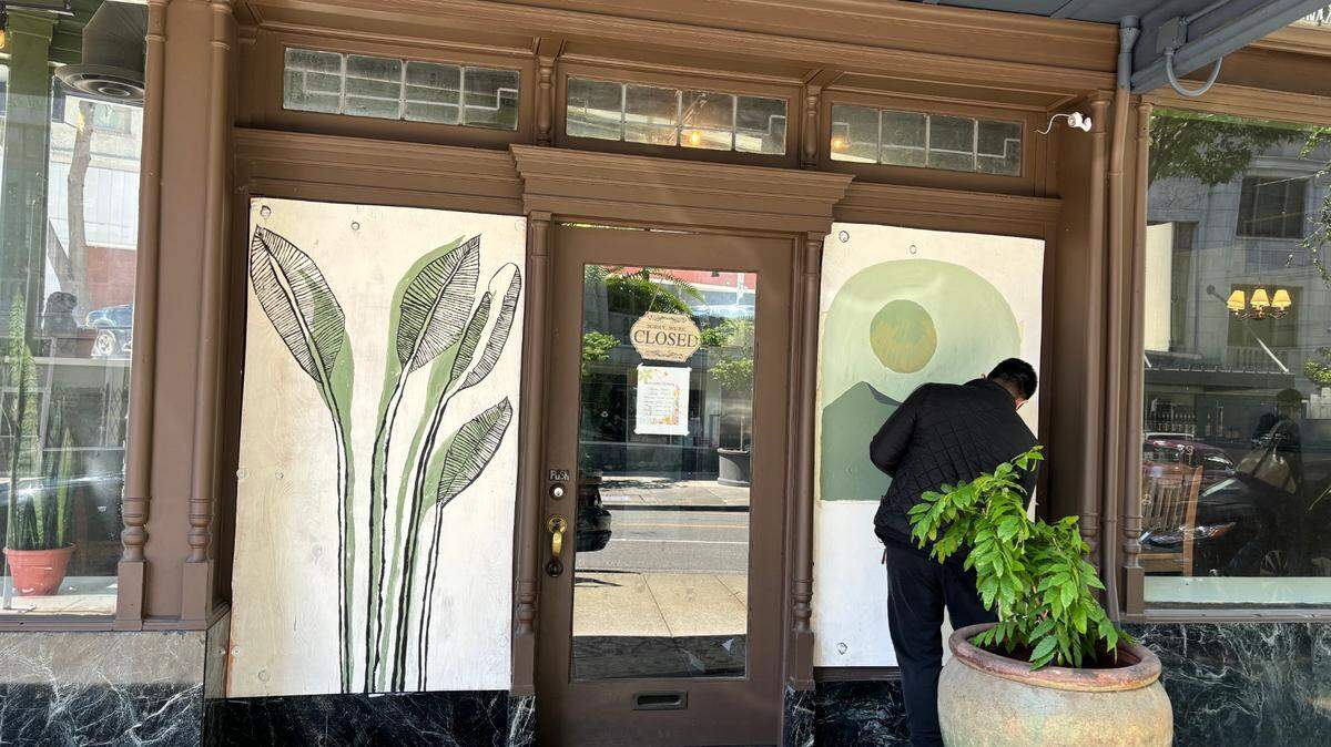 Anh Le, one of the owners of Cremello Cafe, paints over the boards that cover where his windows used to be before they were smashed on Saturday.