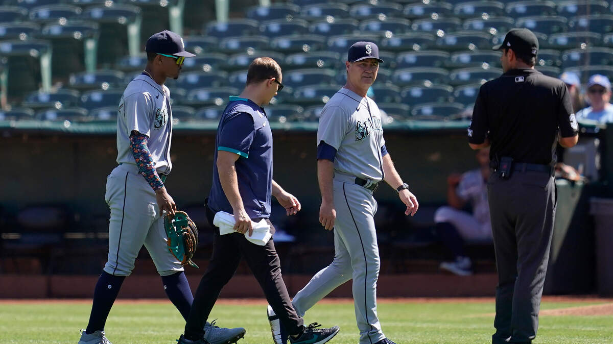 Seattle Mariners center fielder Julio Rodriguez, left, walks off the field with manager Scott Servais, middle right, and a trainer during the first inning of a baseball game against the Oakland Athletics in Oakland, Calif., Thursday, Sept. 22, 2022. (AP Photo/Jeff Chiu)