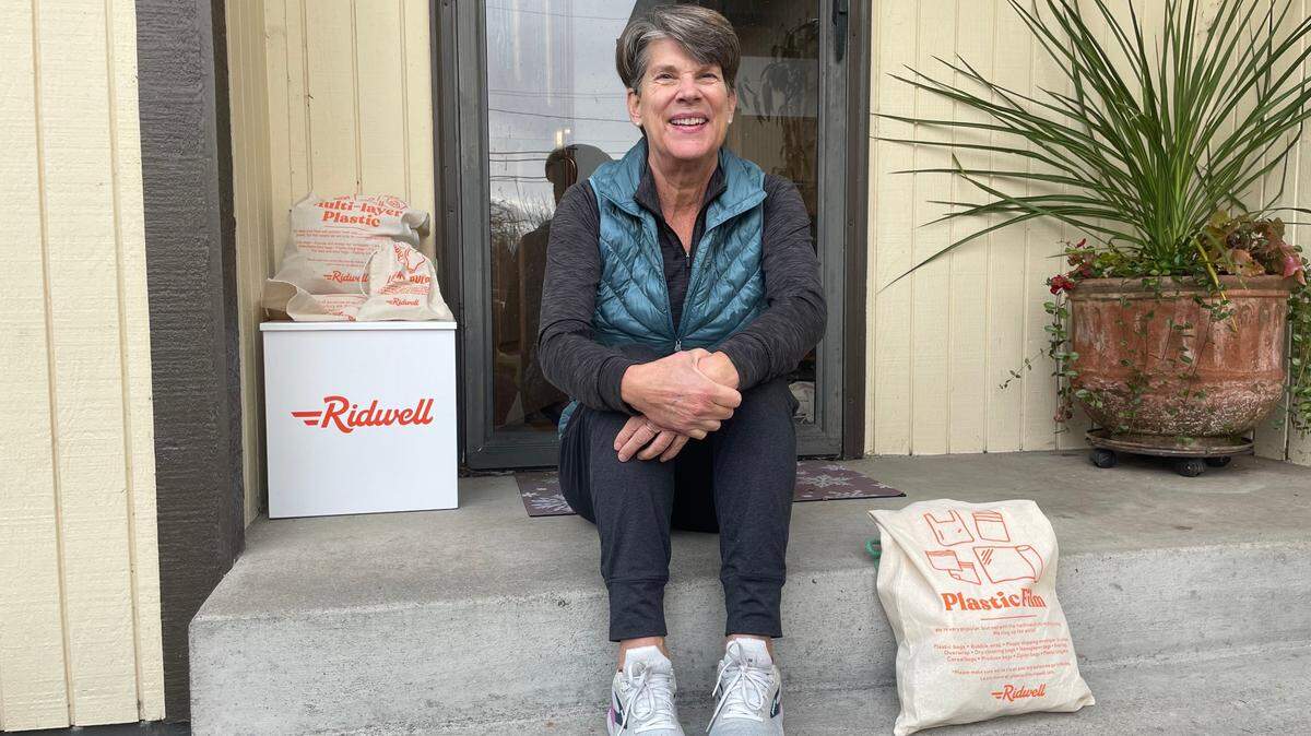 Tacoma resident Nancy Paschall sits on her front stoop on Nov. 12, 2024, next to her Ridwell recycling box, with Ridwell bags she puts various types of plastic in to be recycled.