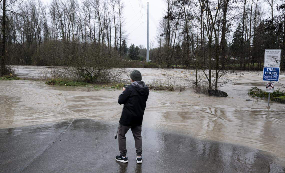 Donald Wagaman takes a photo as fast moving water flows in the Puyallup River as flooding continues along Puyallup Riverwalk Trail, on Thursday, Dec. 11, 2025, in Puyallup, Wash.