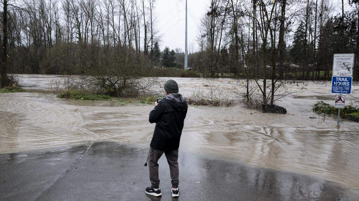 Donald Wagaman takes a photo as fast moving water flows in the Puyallup River as flooding continues along Puyallup Riverwalk Trail, on Thursday, Dec. 11, 2025, in Puyallup, Wash.